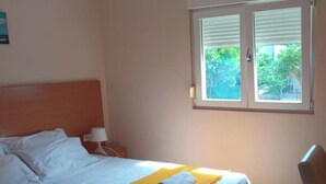 Hotellihuone, jossa on sänky, ikkuna, tuoli ja yöpöytä, jossa on lamppu.