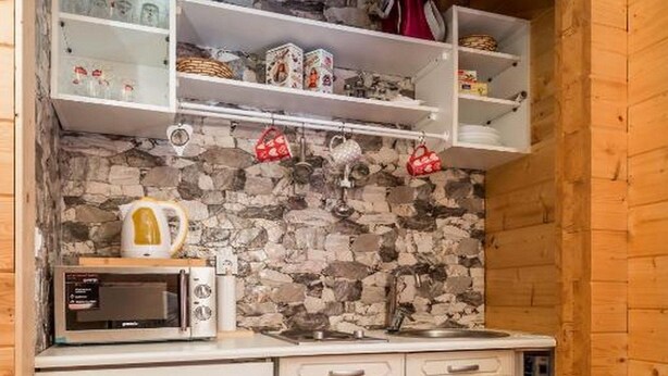 Een kleine keuken met een stenen muur, witte kastjes en een magnetron.