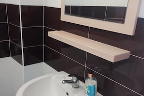 Ein Badezimmer mit einem weißen Waschbecken, einem Spiegel darüber und einem Regal.