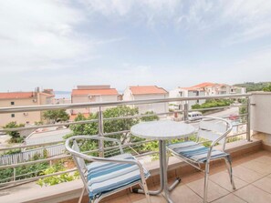 Ein Balkon mit einem runden Tisch und zwei gestreiften Liegestühlen, mit Blick auf ein Wohngebiet mit roten Dächern.
