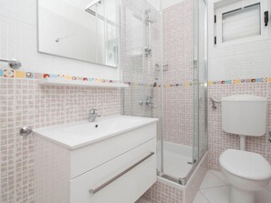 Ein Badezimmer mit weißem Waschbecken, einer Duschkabine aus Glas und einer Toilette.
