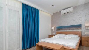 A hotel room with a bed, a bedside table, a bench, an air conditioning unit, and a painting on the wall. - Apartments Antonio - Comfort One-bedroom Apartment With Balcony and Sea View - 4 (Tucepi)