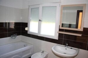 A bathroom with a bathtub, a sink, and a window with blinds. - Apartments Lux Lukić Utjeha - Triple Room (Utjeha)