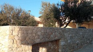 A stone wall with a small opening, possibly for a window or door, in a residential area with trees and a clear sky. - Apartments Lux Lukić Utjeha - Triple Room (Utjeha)