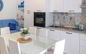 A modern kitchen with white cabinets, a black oven, a stainless steel sink, and a dining table with chairs. - Lovely apartment in Donnalucata with WiFi (Donnalucata)