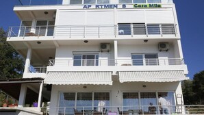 Un edifici de diverses plantes amb balcons, un cartell que diu 'AP RTMEN S Casa Mila' i una zona exterior coberta amb mobles.