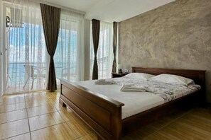 A hotel room with a wooden bed, a balcony with a chair, and a view of the outdoors. - Casa Mila Apartments - Studio apartment with sea view (Ulcinj)