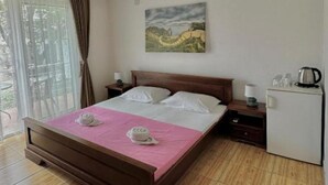Habitació d'hotel amb llit, una tauleta de nit, un petit frigorífic i una finestra amb cortines.