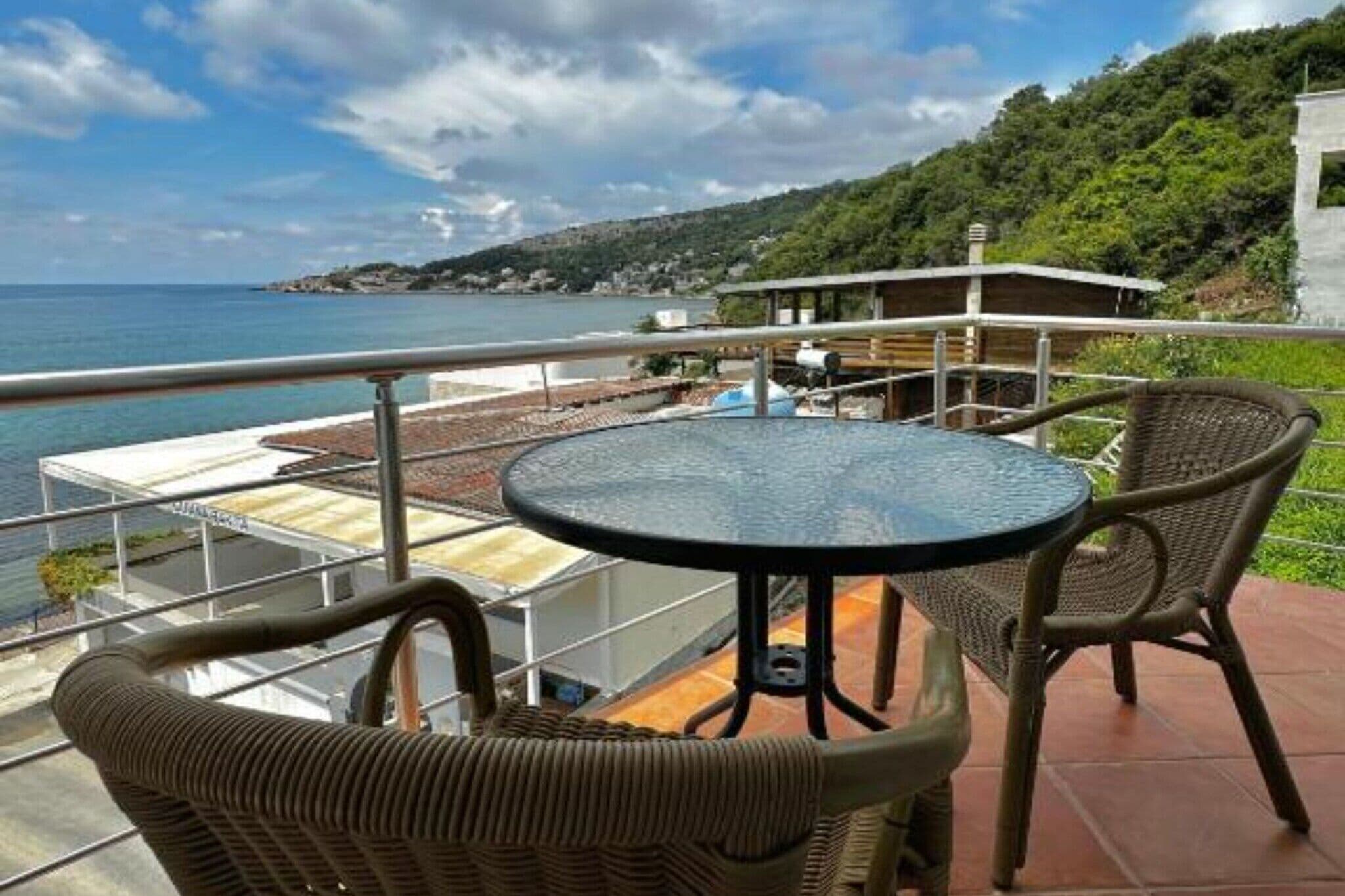 Un balcón con mobiliario de mimbre, una mesa redonda y vistas al mar y las colinas.