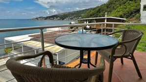 Un balcó amb mobiliari de vimet, una taula rodona i vista al mar i a les muntanyes.