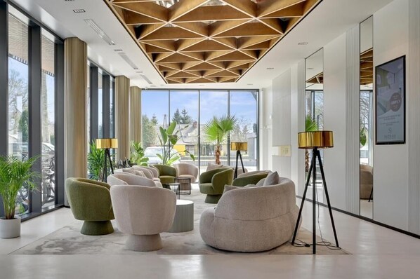 A modern interior with large windows, a geometric ceiling design, and a seating area with sofas and a floor lamp.