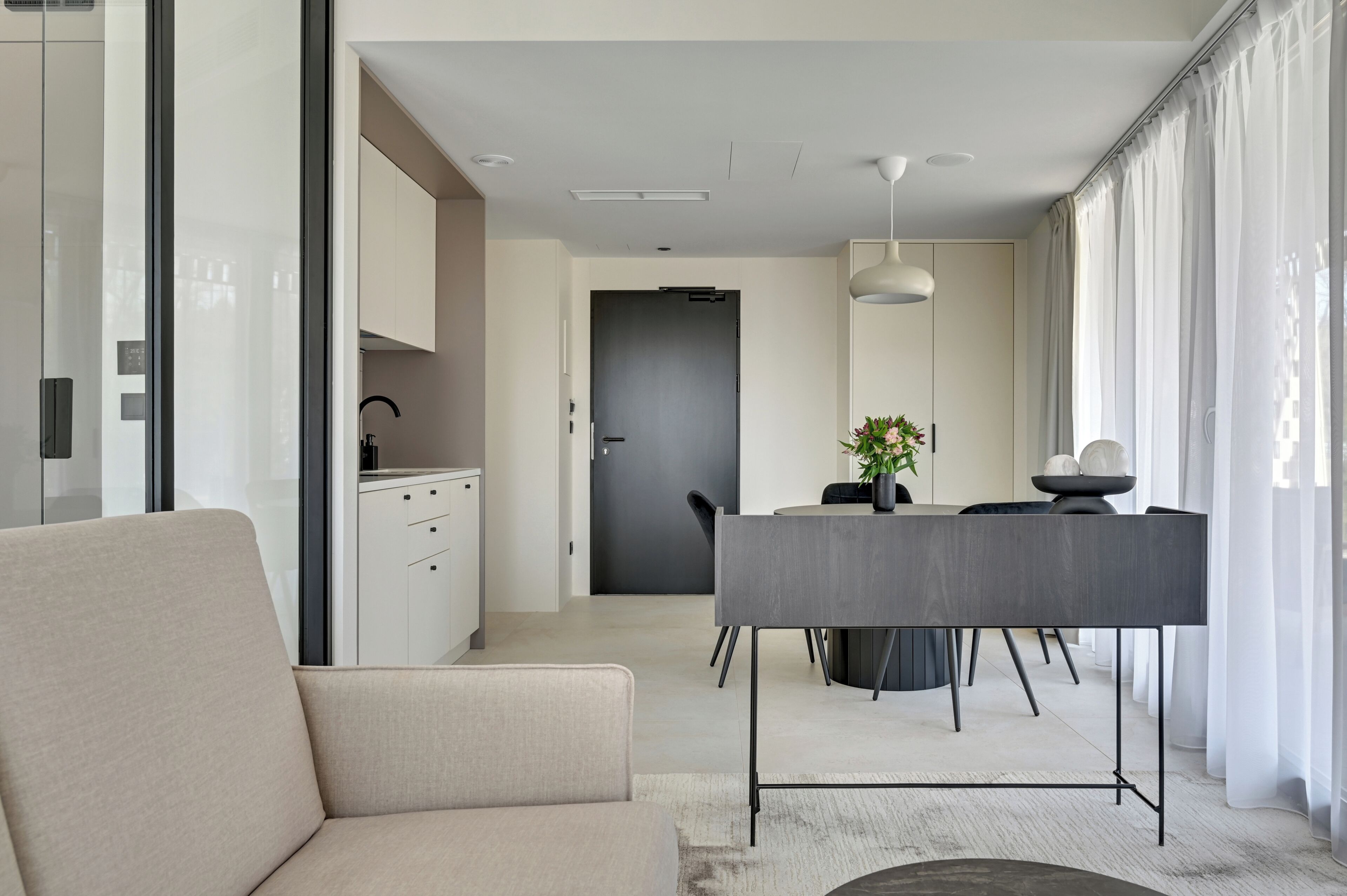 Una sala de estar moderna con un sofá, una zona de comedor con mesa y sillas, y una cocina con armarios y un lavamanos.