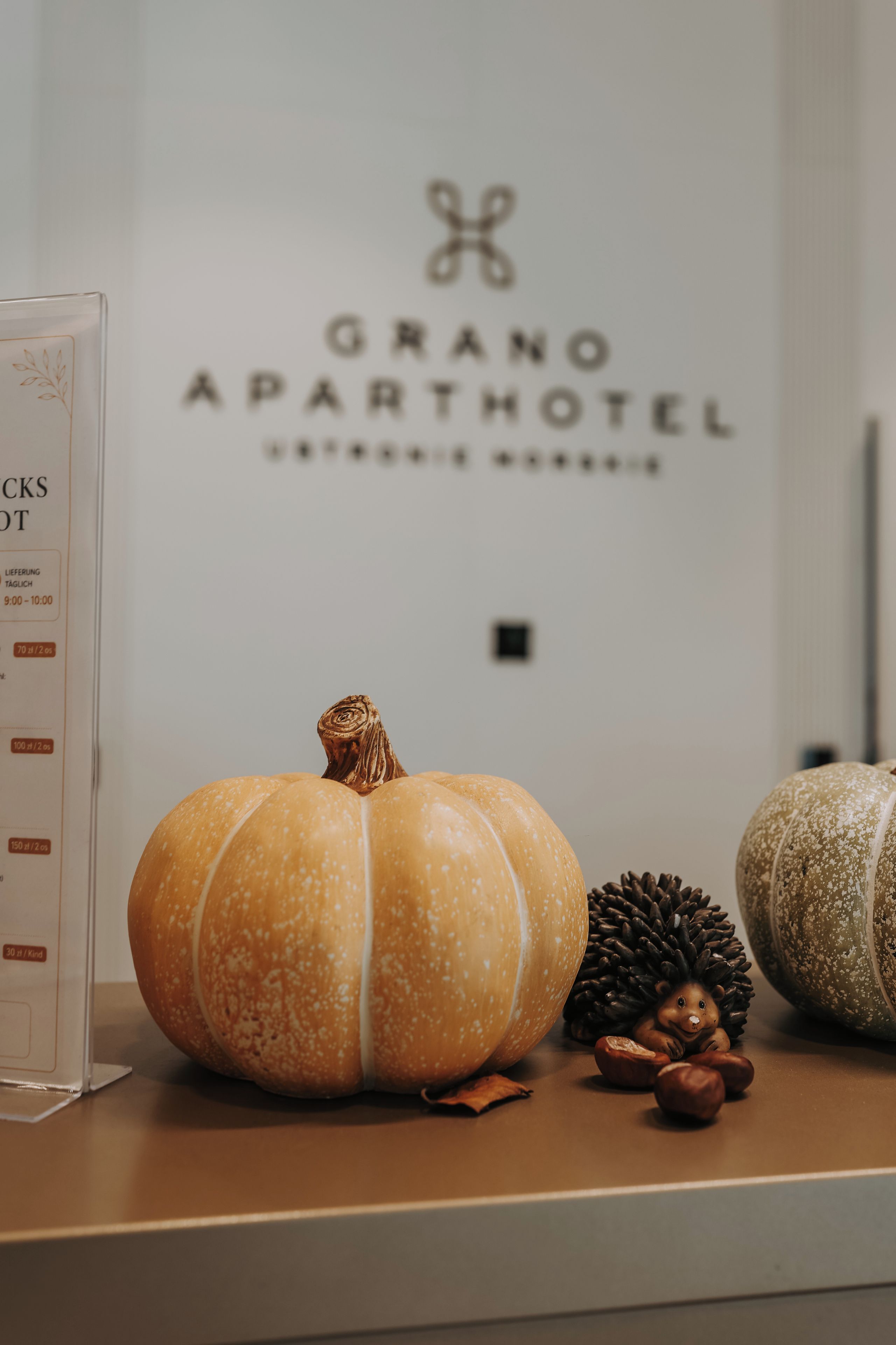 Une table décorée de petites citrouilles et d’une pomme de pin, et un mur sur lequel on peut lire le texte « GRANO APARTHOTEL ».