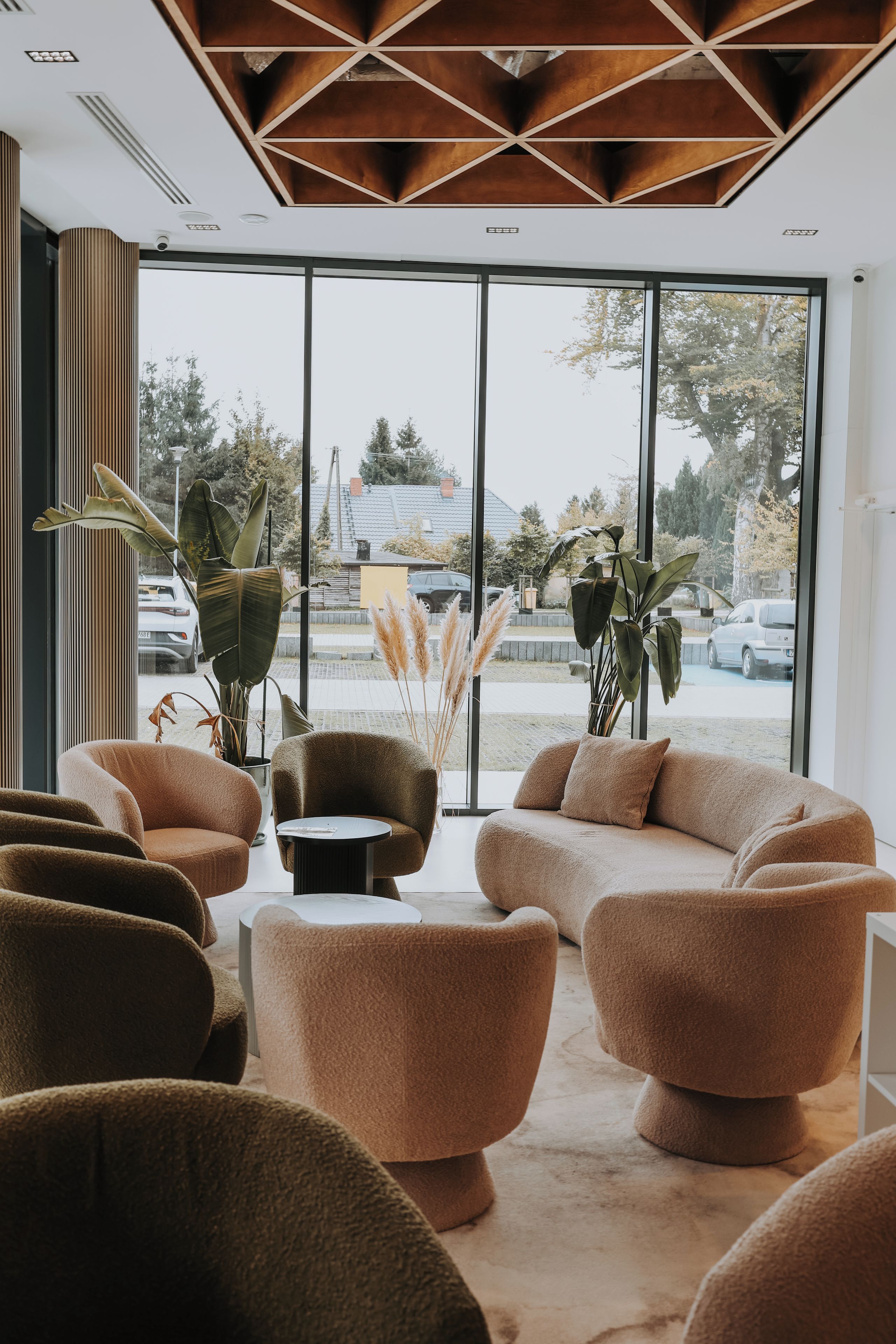 Un interior moderno con una zona de estar que incluye sofás y sillones, ventanas amplias con vistas al exterior y un techo con diseño geométrico.
