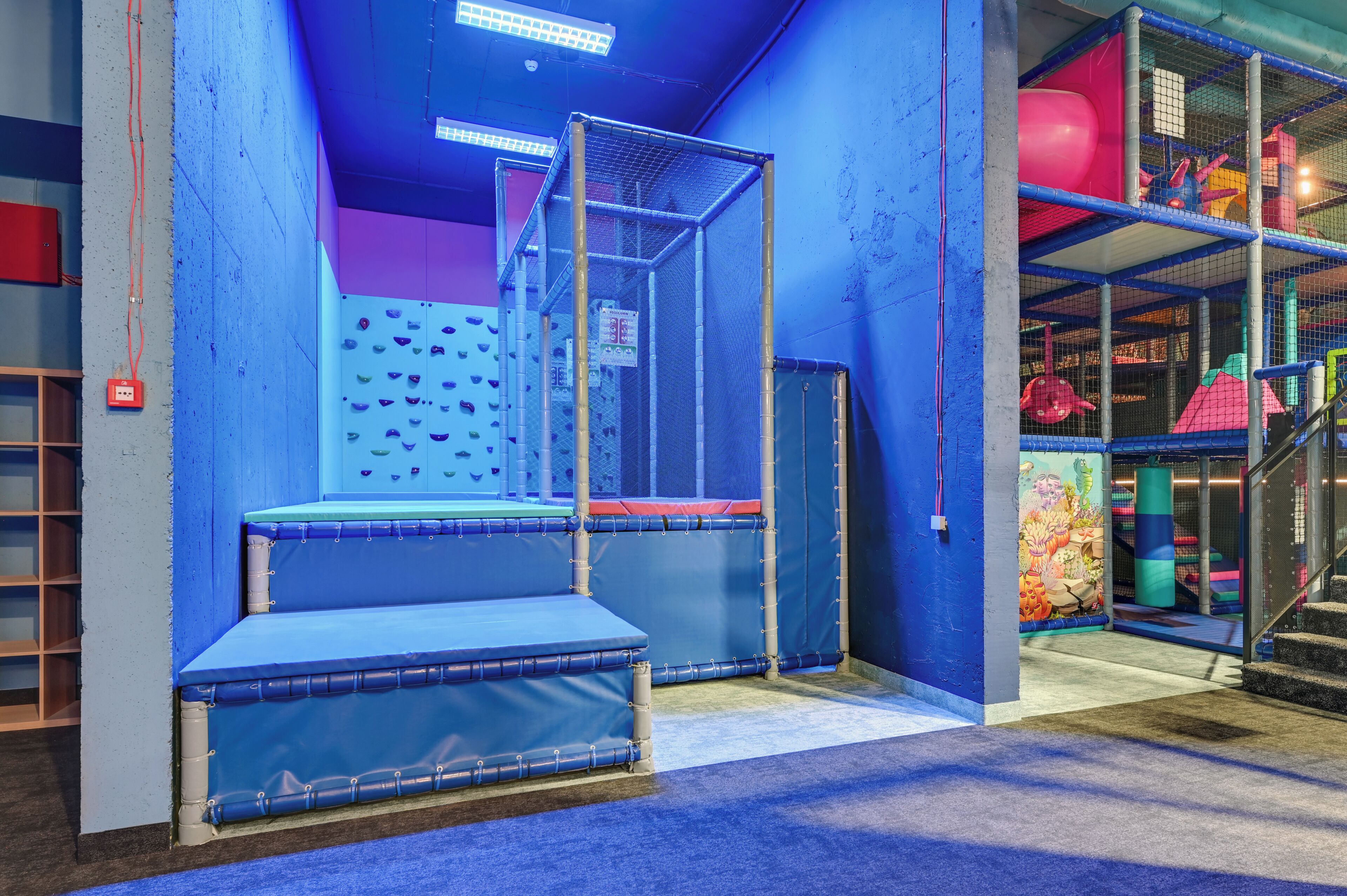 An indoor play area with climbing walls, padded seating, and a netted enclosure.