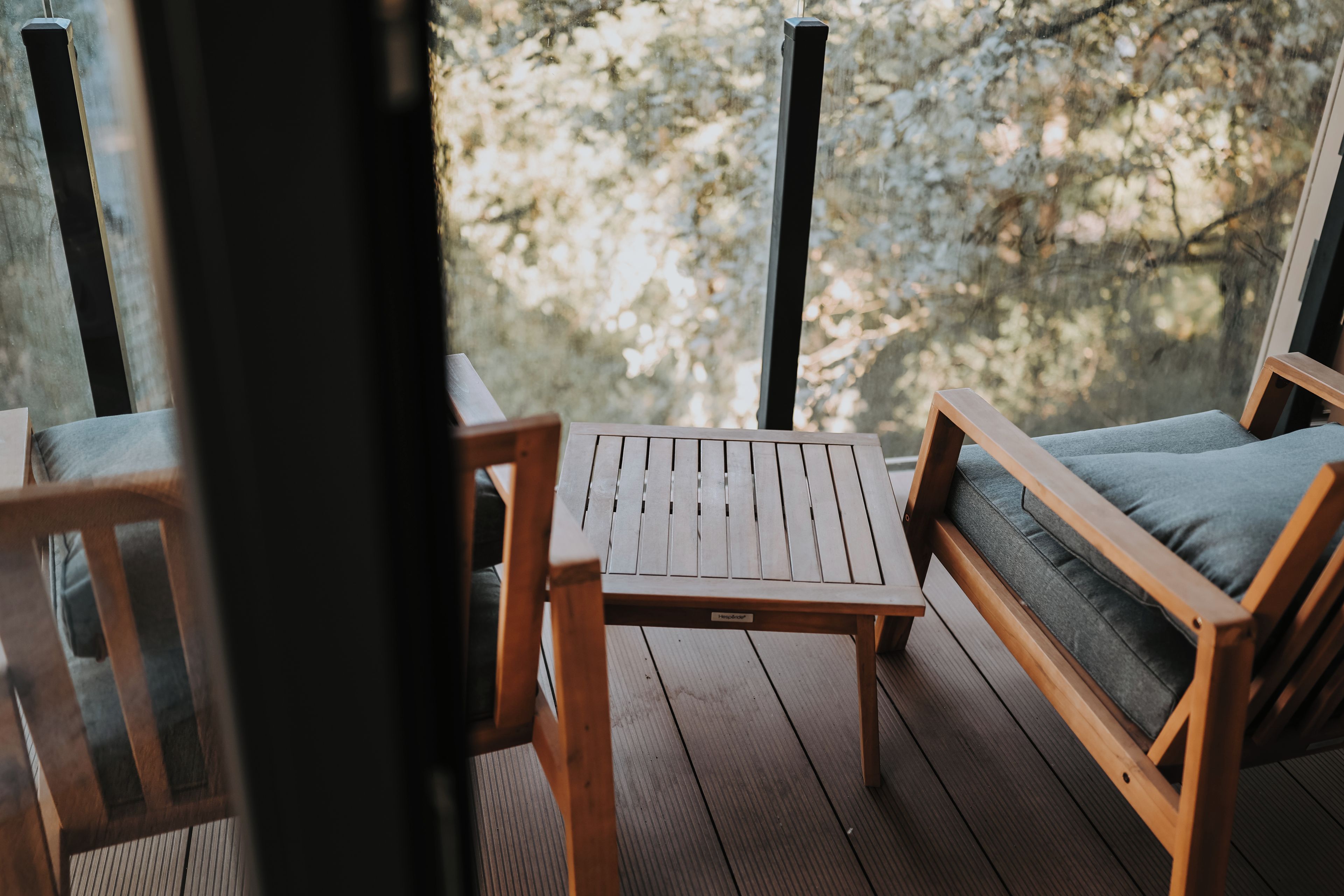 Una terraza de madera con una mesa y dos sillas, una de ellas con cojín.