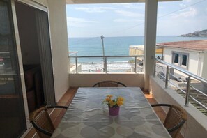 Un balcón con mesa y sillas, con vista a la costa, edificios y un cielo despejado.
