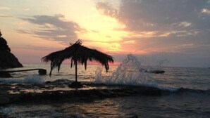 A beach scene with a thatched structure and waves crashing onto the shore. - Casa Mila Apartments - Studio apartment with sea view (Ulcinj)
