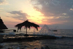 A beach scene with a thatched structure and waves crashing onto the shore. - Casa Mila Apartments - Studio apartment with sea view (Ulcinj)