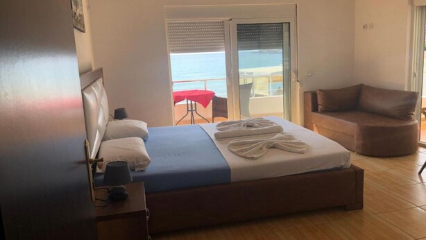A hotel room with a bed, a chair, a table with a red tablecloth, and a view of the sea through a sliding door. - Casa Mila Apartments - Studio apartment with sea view (Ulcinj)