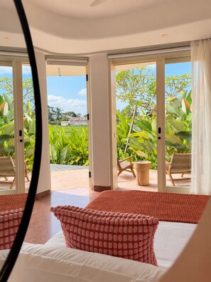 A hotel room with a bed, a view of a garden, and a door leading outside. - Villa Merah Merah Ubud by Fays Hospitality (Kabupaten Gianyar)