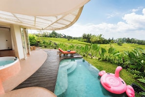 Uma área de piscina com hidromassagem e espreguiçadeiras, cercada por vegetação exuberante e vista para campos em socalcos.