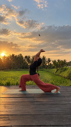 A person performing a yoga pose on a mat in an outdoor setting with a sunset in the background. - Villa Merah Merah Ubud by Fays Hospitality (Kabupaten Gianyar)