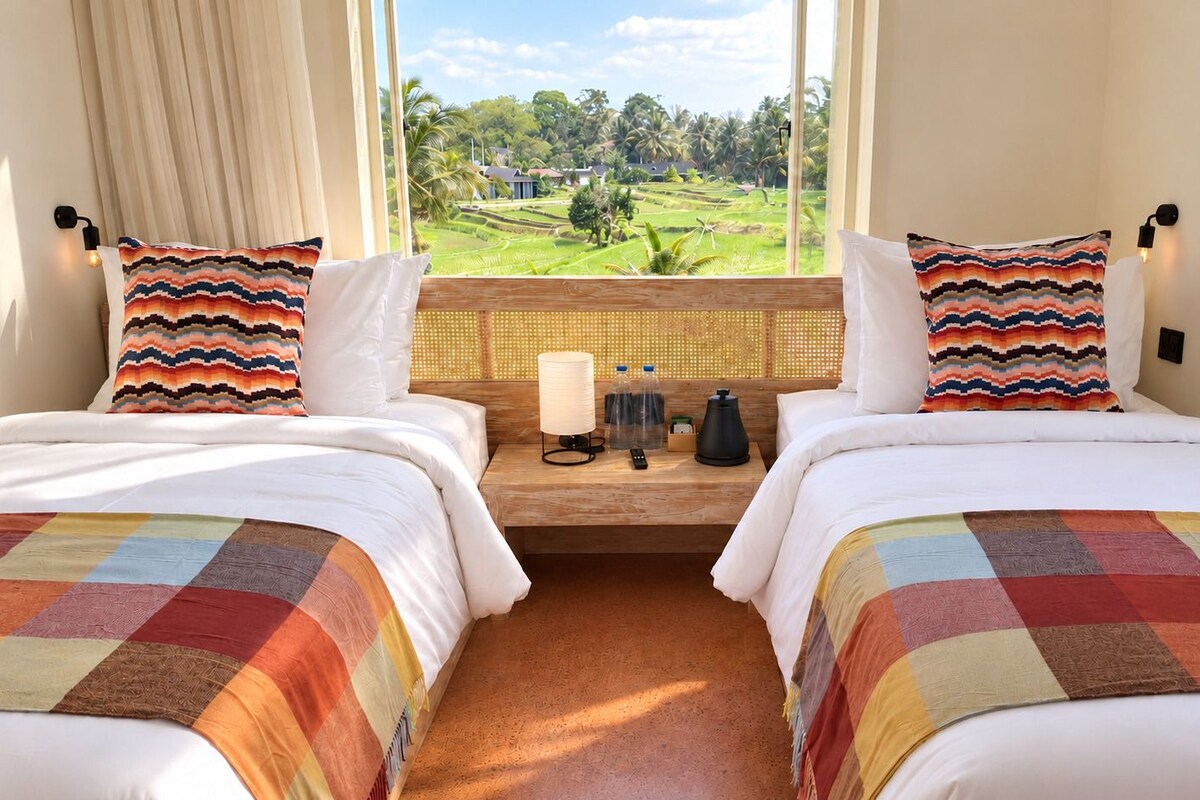 A double room with two beds, a window with a view of a green landscape, a bedside table with a lamp, and a kettle.