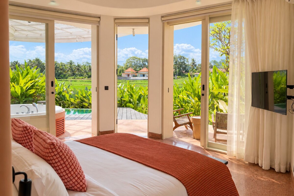 A bedroom with a large bed, a TV, and a view of a pool and greenery.