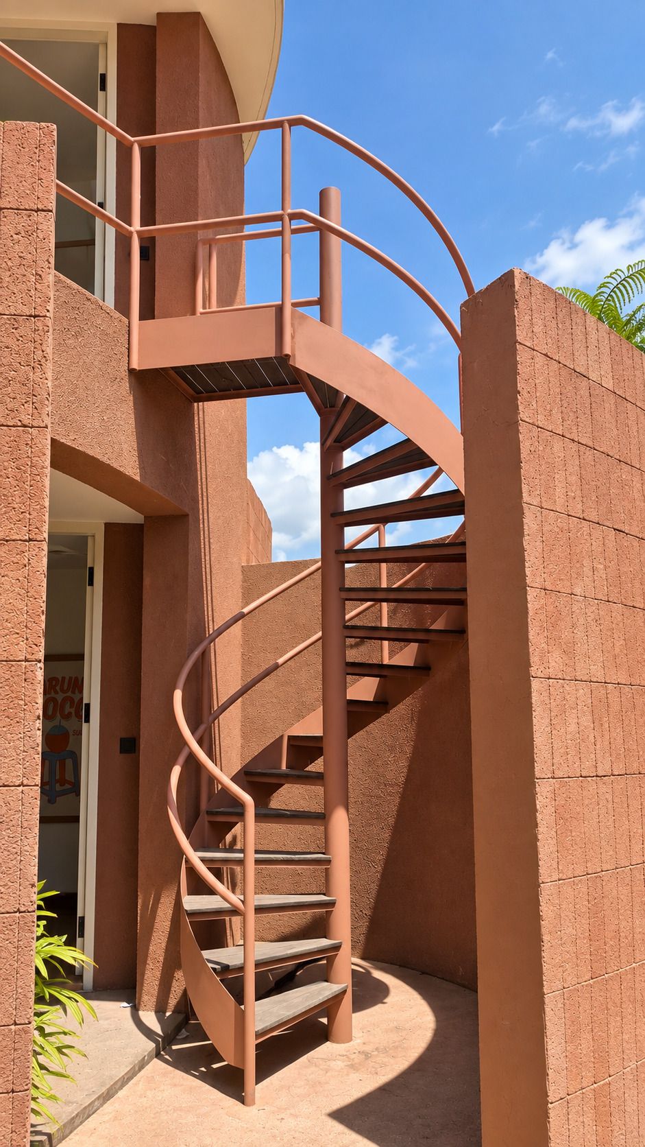 Una escalera de caracol con barandilla de metal que conduce a un piso superior, junto a un edificio con fachada de ladrillo.