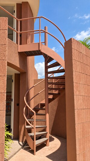 A spiral staircase with a metal railing, leading to an upper floor, adjacent to a building with a brick facade. - Villa Merah Merah Ubud by Fays Hospitality (Kabupaten Gianyar)