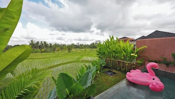 Un área de piscina con un flotador con forma de flamenco rosa, rodeada de exuberante follaje y vistas a terrazas de cultivo de arroz.