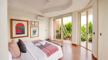 Un dormitorio con una cama grande, un ventanal corredizo que da a un balcón con plantas y cuadros decorativos en la pared.
