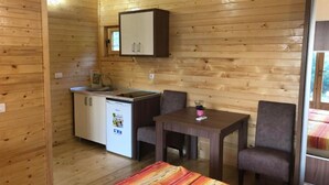 Een kleine kamer met een kitchenette, een eettafel en twee stoelen, en een bed.