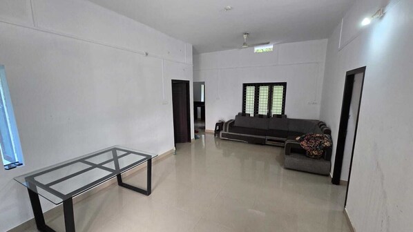 A spacious room with a glass-top table, a sofa, and a window with blinds.