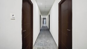 A long, narrow hallway with white walls and dark wooden doors on both sides. - Collection O Atlas DLF Formerly Hillside (Hyderabad)