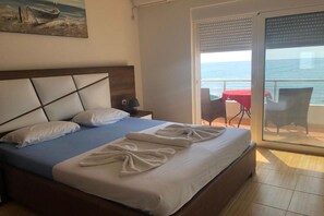 A hotel room with a bed, a nightstand, a painting, a balcony with a table and chairs, and a view of the sea. - Casa Mila Apartments - Standard Triple bedroom with sea view (Ulcinj)