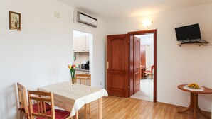 A dining area with a table, chairs, a small table with bananas, a TV on a stand, and a kitchen visible through an open door. - Apartments Ana Lopud - One-bedroom Apartment With Balcony and Sea View - 4 (Dubrovnik)