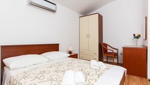 A hotel room with a bed, a wardrobe, a desk with a chair, and a bedside table with a lamp. - Apartments Ana Lopud - One-bedroom Apartment With Balcony and Sea View - 4 (Dubrovnik)