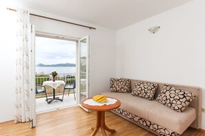 Ein Zimmer mit einer Couch, einem kleinen Tisch mit Bananen, Meerblick und einem Balkon mit Stühlen und Tisch.