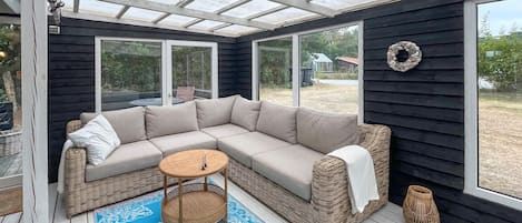 A covered outdoor seating area with a sectional sofa, a round table, and a patterned rug.