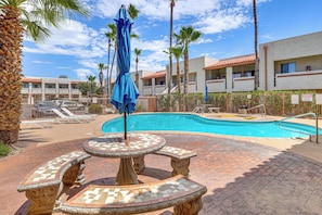 Une piscine avec une terrasse carrelée, des chaises longues et des palmiers.