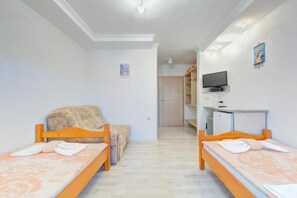 A room with two wooden beds, a sofa, a television on a stand, and a door leading to another room. - Glory Sanctuary Retreat - Twin room with balcony 2 (Medugorje)