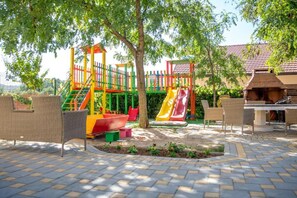 A playground with slides and climbing structures, surrounded by wicker furniture and a barbecue area. - Glory Sanctuary Retreat - Twin room with balcony 2 (Medugorje)