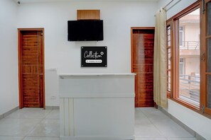 A reception area with a flat-screen TV mounted above a reception desk, wooden doors, and a large window with a view of the outside. - Super Collection O by OYO Nayagaon Vikas (Kharar)