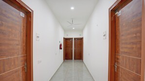 Un pasillo con puertas de madera numeradas del 101 al 104, un ventilador de techo y un extintor.