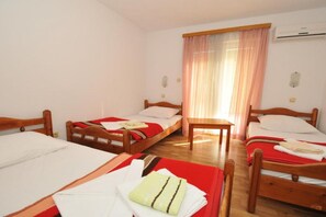 A hotel room with three wooden beds, a small table, and a window with sheer curtains. - Glory Sanctuary Retreat - Triple Room with Balcony (Medugorje)