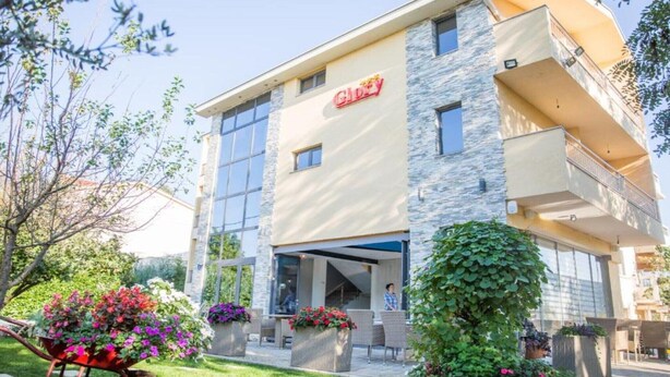 A multi-story hotel with a stone facade, large windows, and a covered entrance. - Glory Sanctuary Retreat - Triple Room with Balcony (Medugorje)