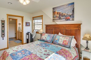 A bedroom with a large bed, a wooden headboard, a painting of a snowy town, and a window with a view of the outdoors. - Yellowstone Basecamp! Emigrant Home w/ Mtn Views (Emigrant)