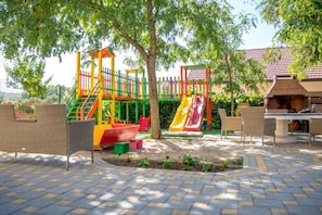 Ein Spielplatz mit Rutschen und Klettergerüsten, umgeben von Korbmöbeln und einem Grillplatz.